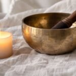 Tibetan healing bowl and candle on white linen cloth